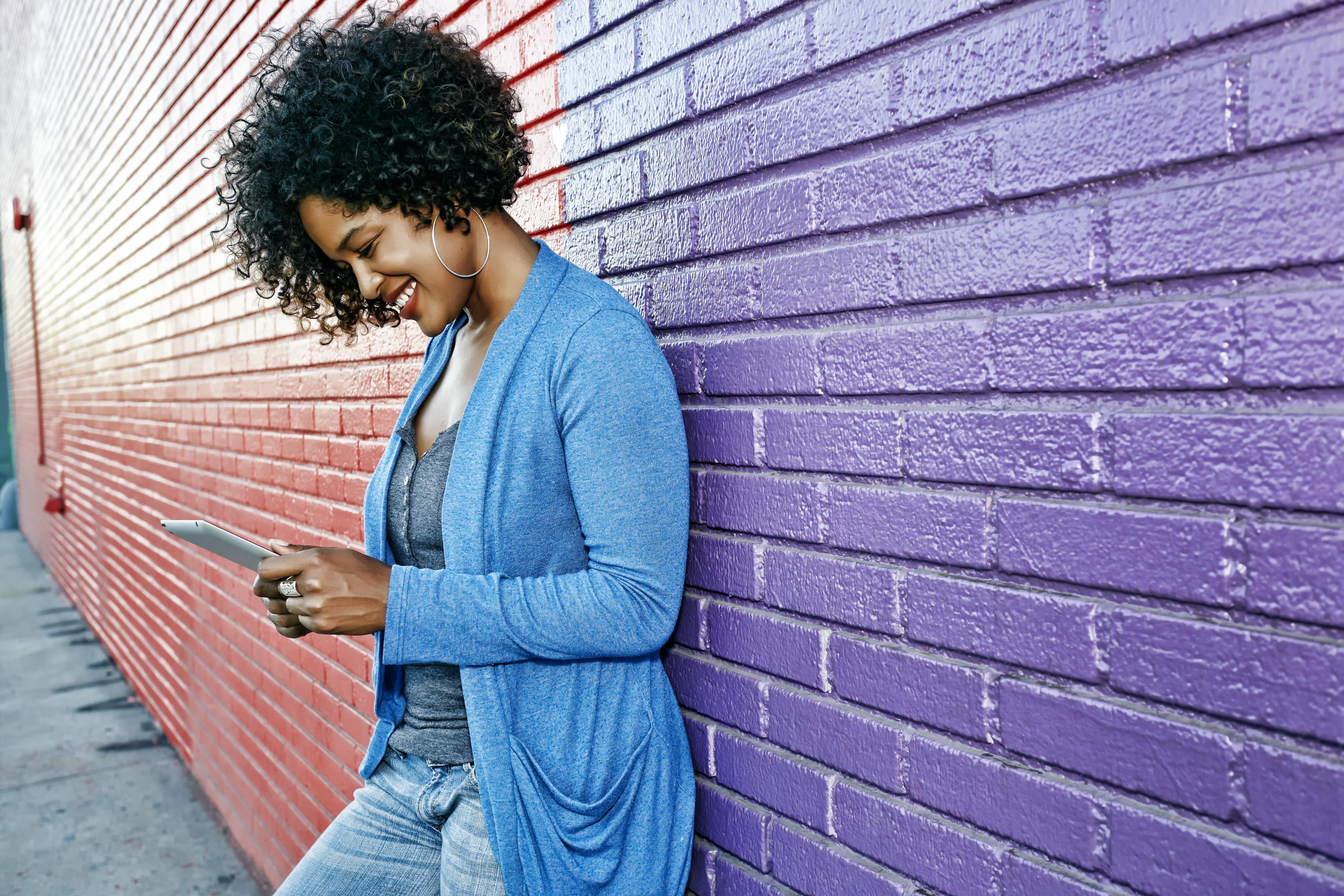 Mixed race woman with cell phone standing by colorful wall